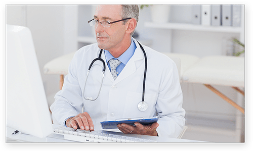Мъж-лекар, който държи диаграма на пациента и гледа екрана на компютъра.